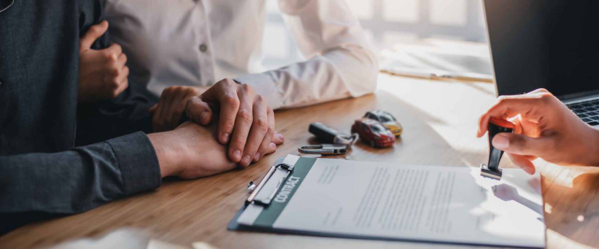 couple sit at table with arms linked as person stamps contract