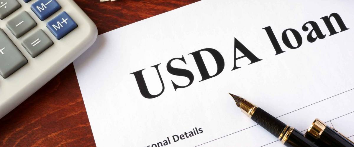 USDA loan form with ballpoint pen on top, calculator beside it