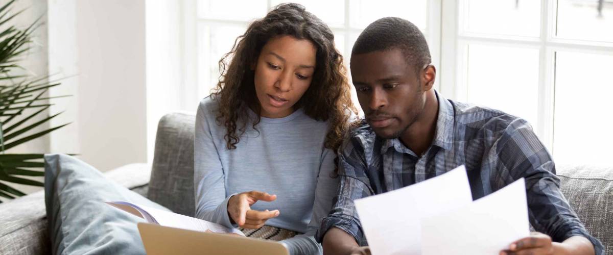 serious couple look at papers and computer screen while sitting on a couch