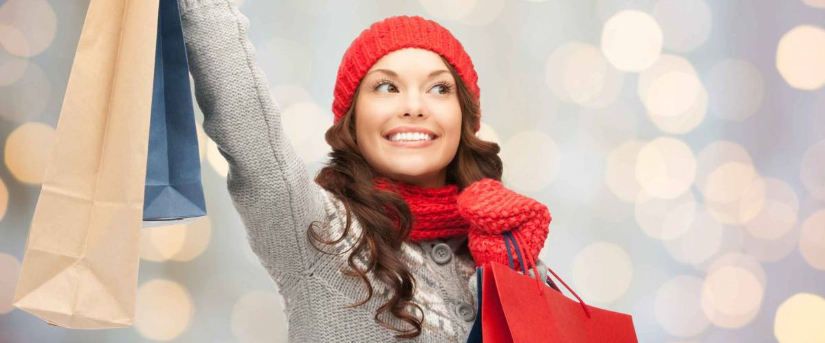 happy young woman in winter clothes with shopping bags over lights background