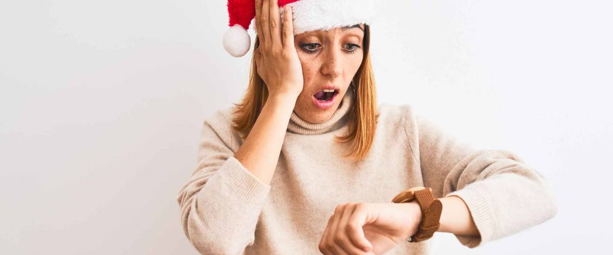 Beautiful redhead woman wearing christmas hat over isolated background Looking at the watch time worried, afraid of getting late
