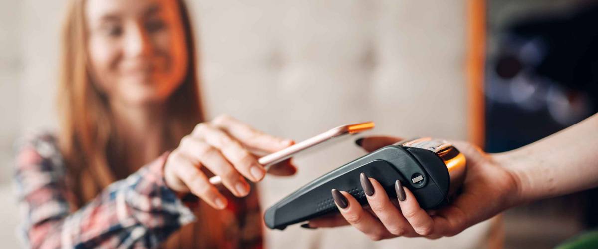 Young woman pay by mobile phone in cafe