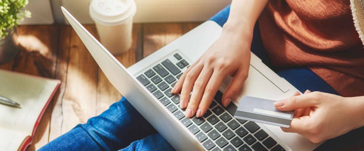 woman holding credit card while she types into laptop on her lap
