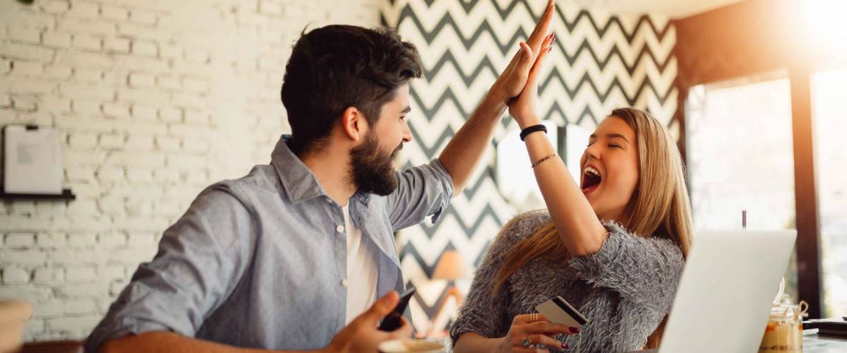 Portrait of an excited young couple giving high five while shopping online.