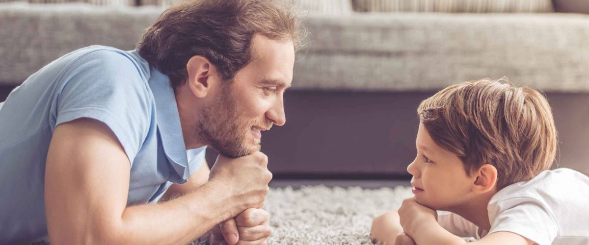 Side view of handsome father and his cute son looking at each other and smiling while spending time together at home