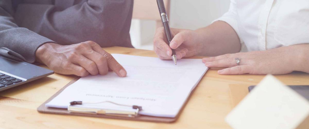 woman holds pen and signs paper while man points at something