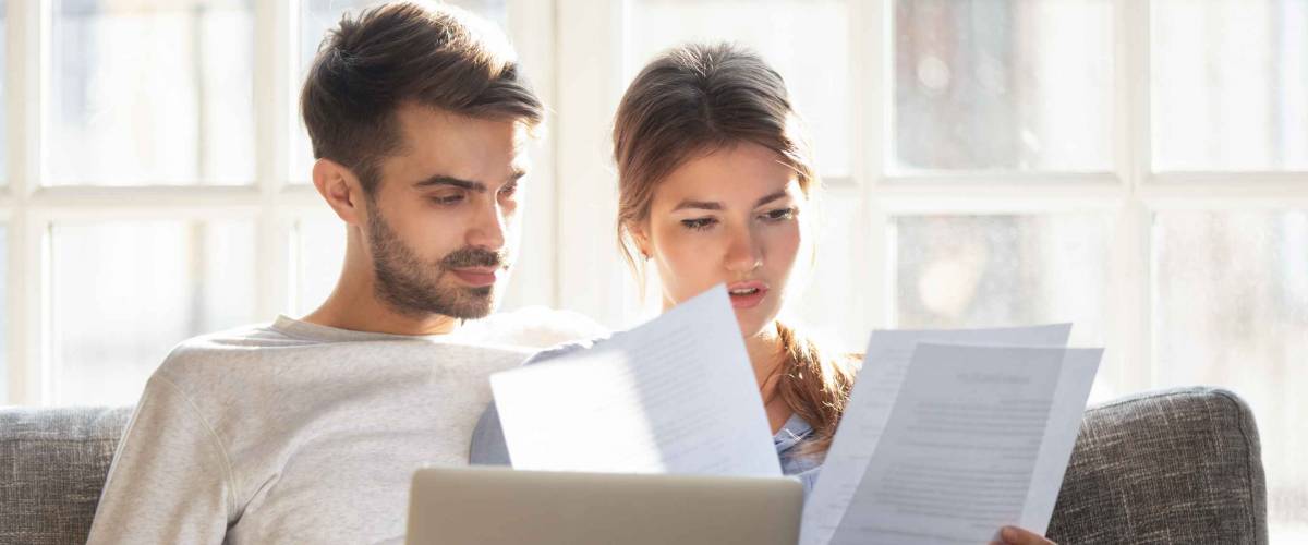 young couple sits on a couch and looks at papers