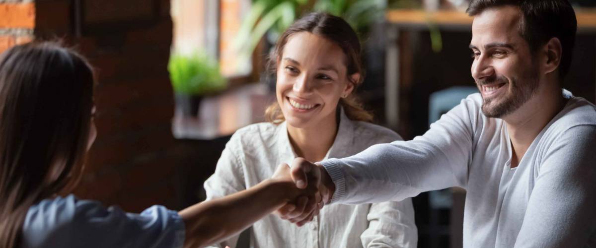 Smiling couple, man shakes hands with another woman across the table