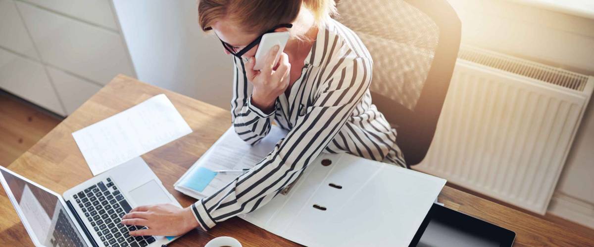 woman working at desk with cellphone to ear, shown from above