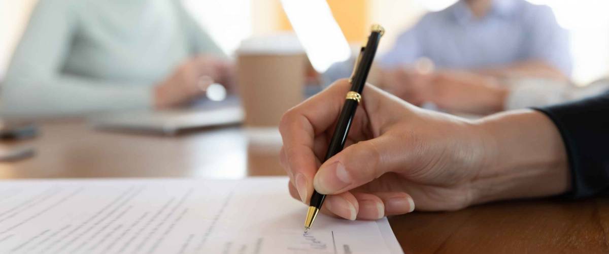 man signs contract with two people sitting in the background