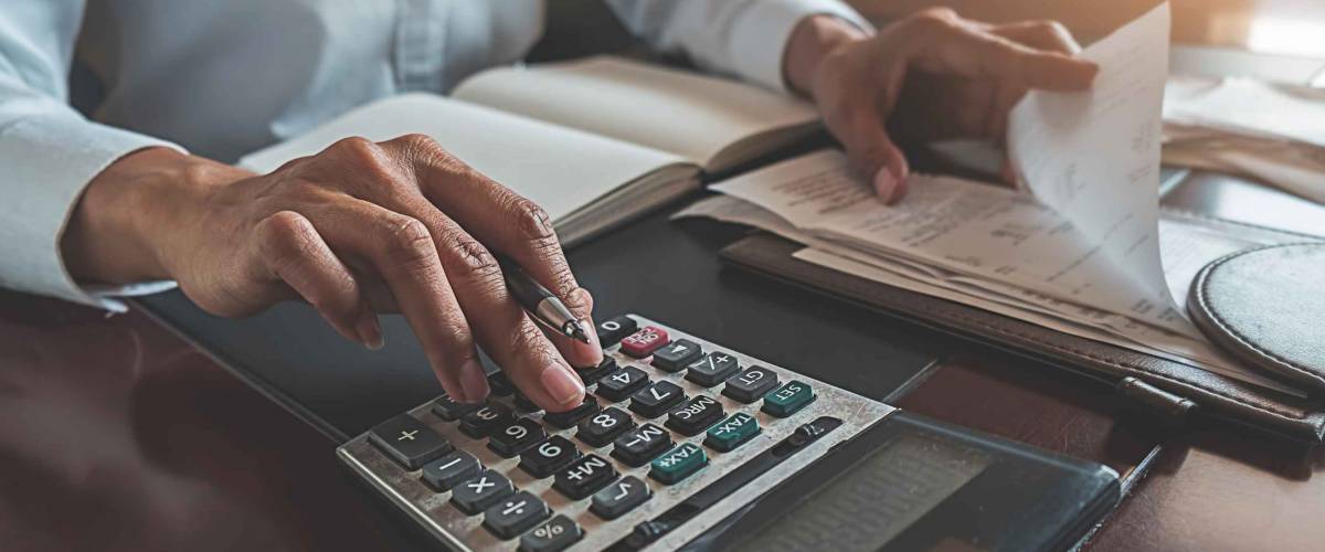 woman's hands flip through papers and add up numbers on calculator