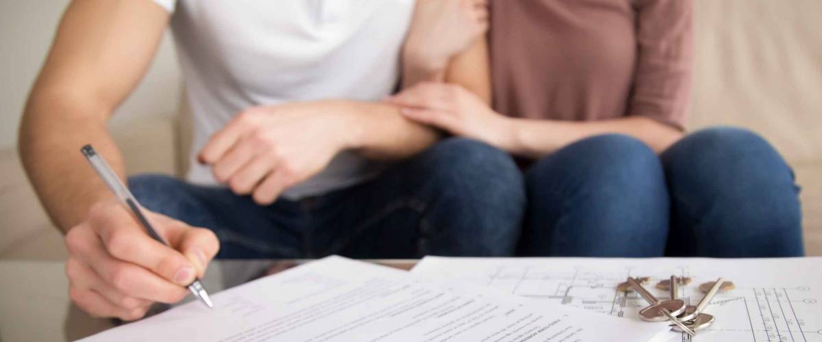 Close up of two people sitting on couch, from chest down, man is is signing a piece of paper