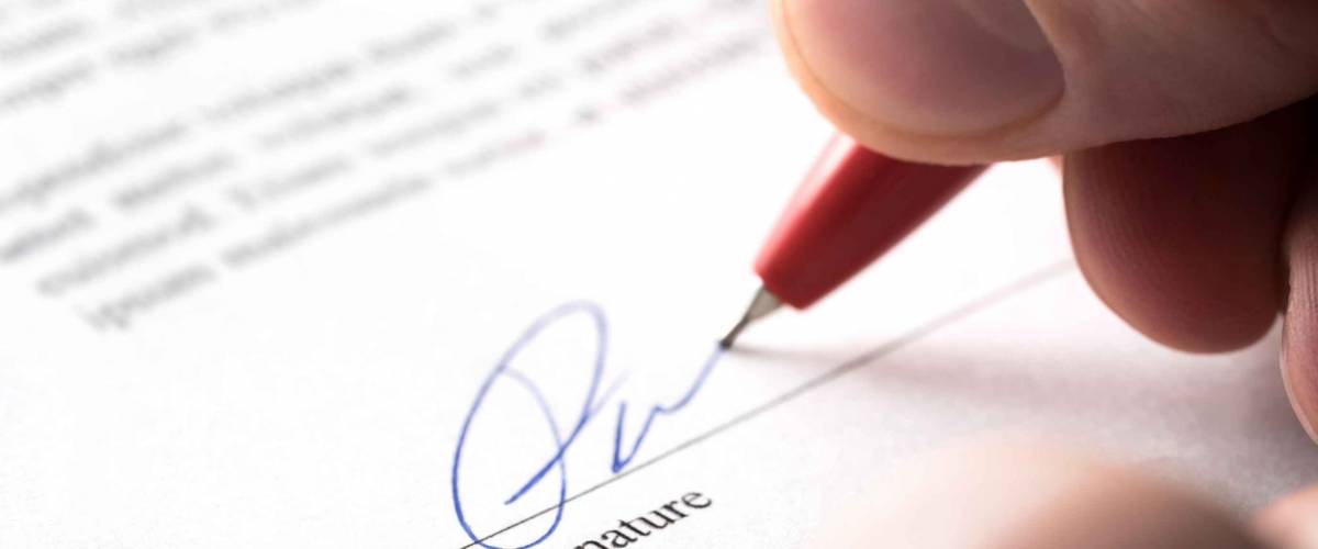 close up of hand holding pen to paper, signing signature