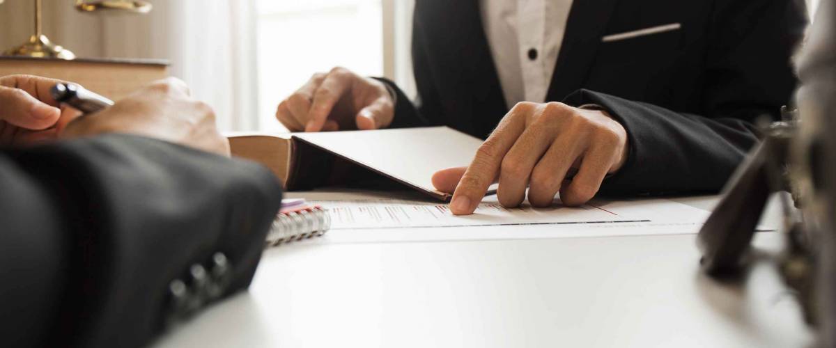 lawyer sits at desk and points to paper, while person sits across from him
