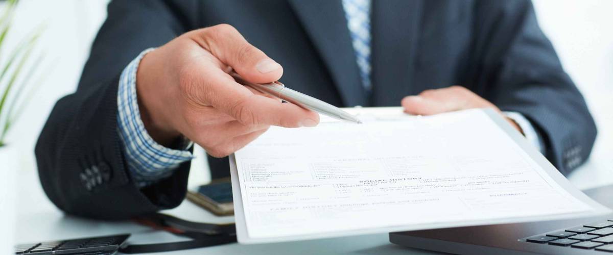 Man in a suit offers to sign a contract holding a pen and documents for signature