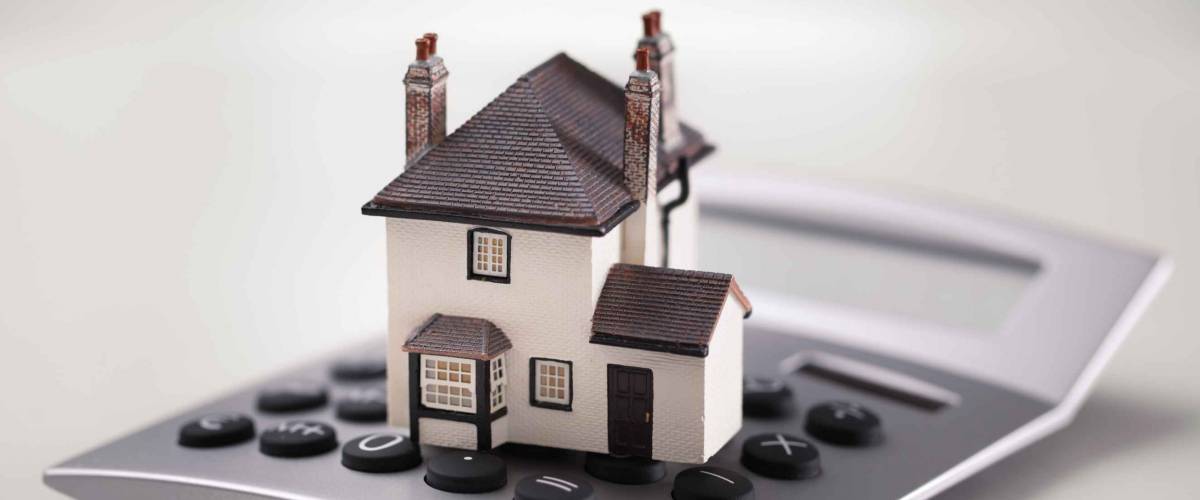 House resting on calculator concept for mortgage calculator, home finances or saving for a house