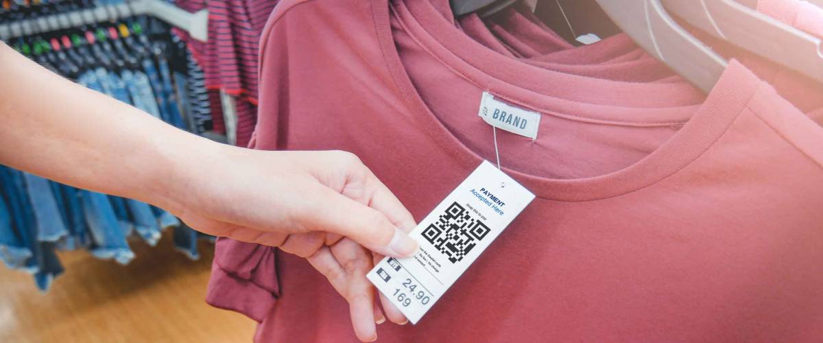 Woman's hand with a cloth hang tag label with QR code in a clothing shop lighting effect.