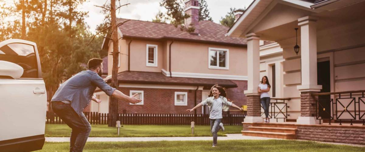Happy family. Dad came home, daughter is running to meet him while wife is waiting on the house's porch.