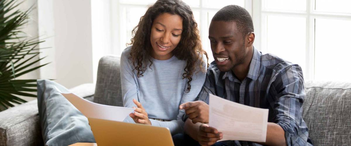 Black couple sitting on sofa at home read documents