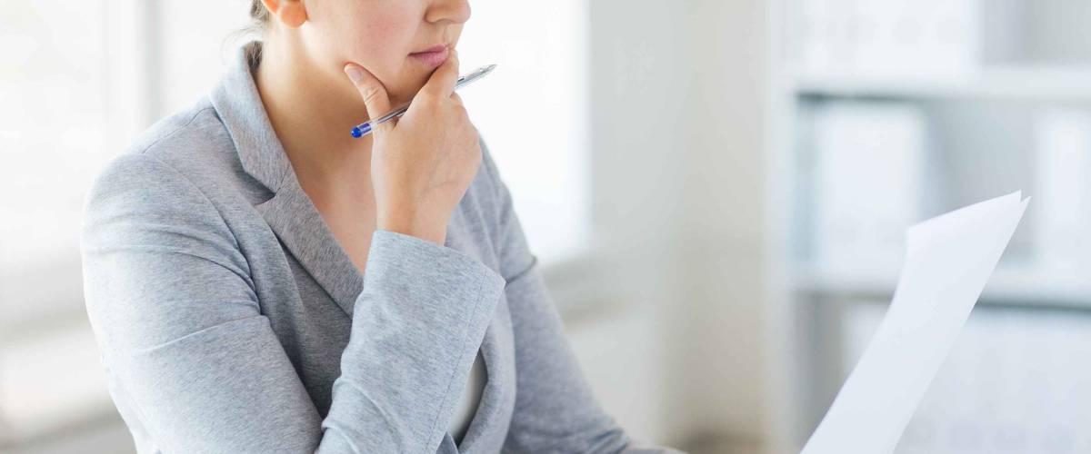 woman contemplating paper in her hand with other hand on chin