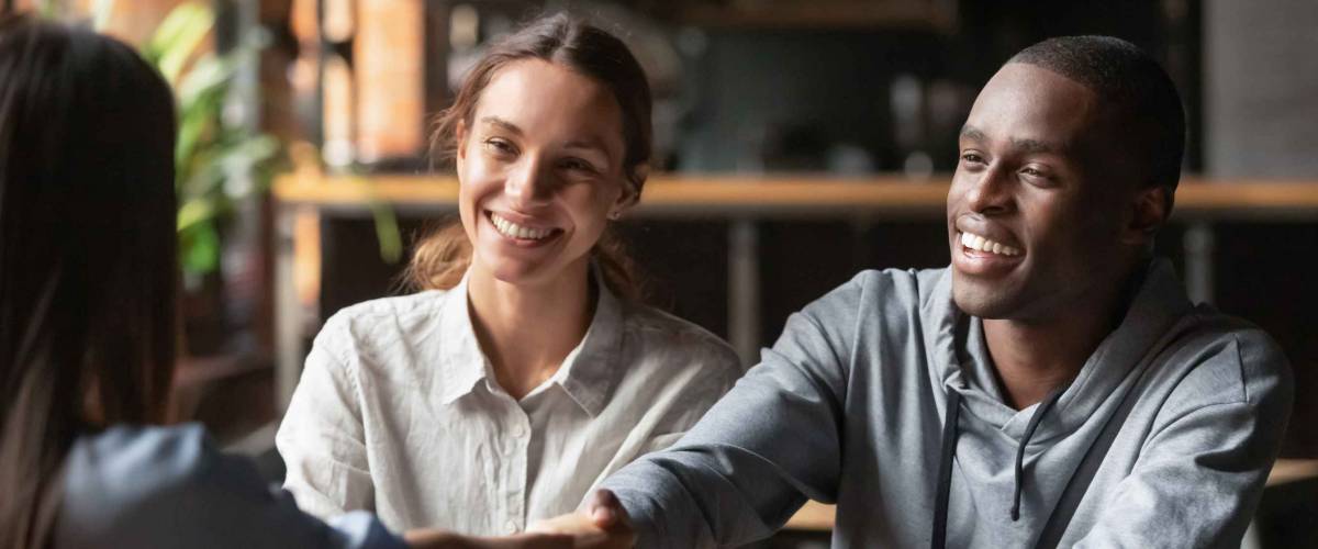 happy young couple in office shake hands with woman across a table