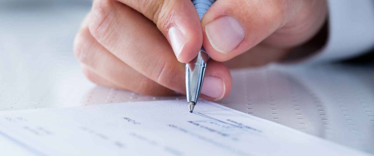 A Male Hand Filling Out The Amount On A Cheque