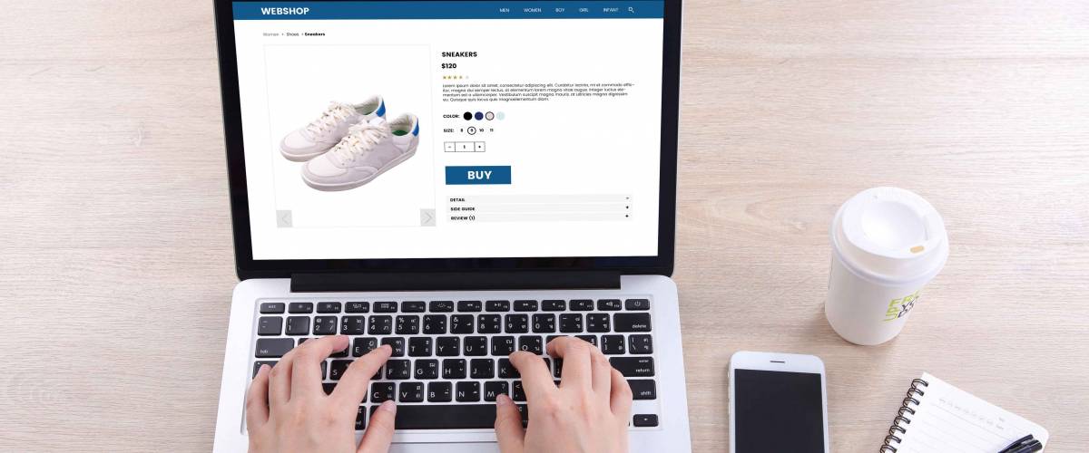 Top view business woman buying sneakers on ecommerce website with smart phone and coffee on wooden desk