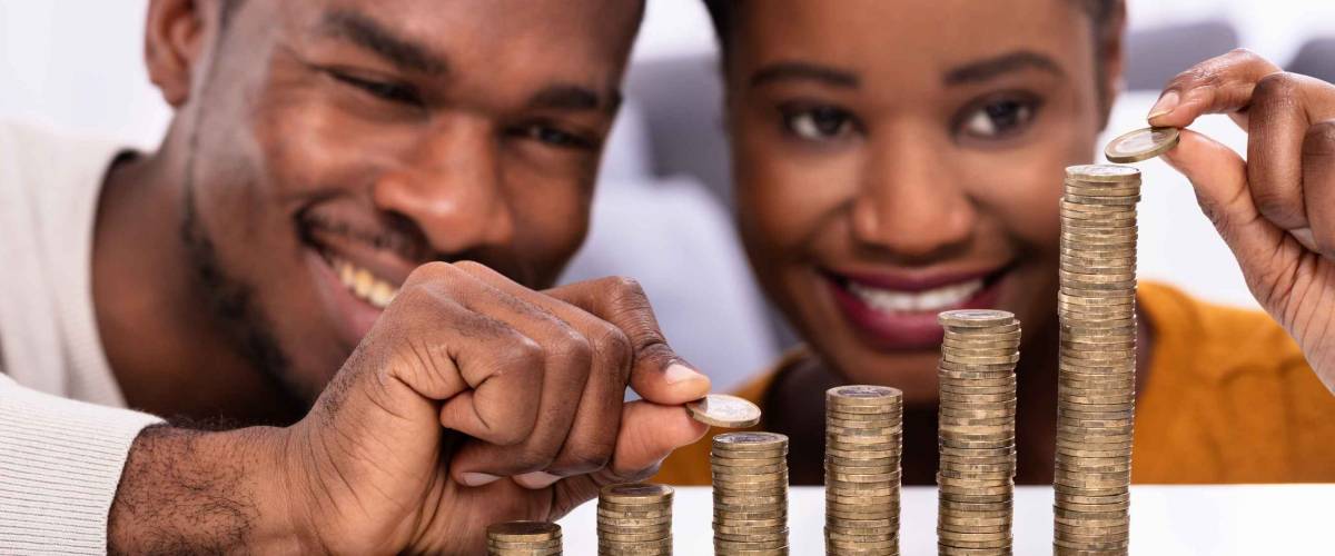 Happy African Couple Stacking Coins Over White Desk