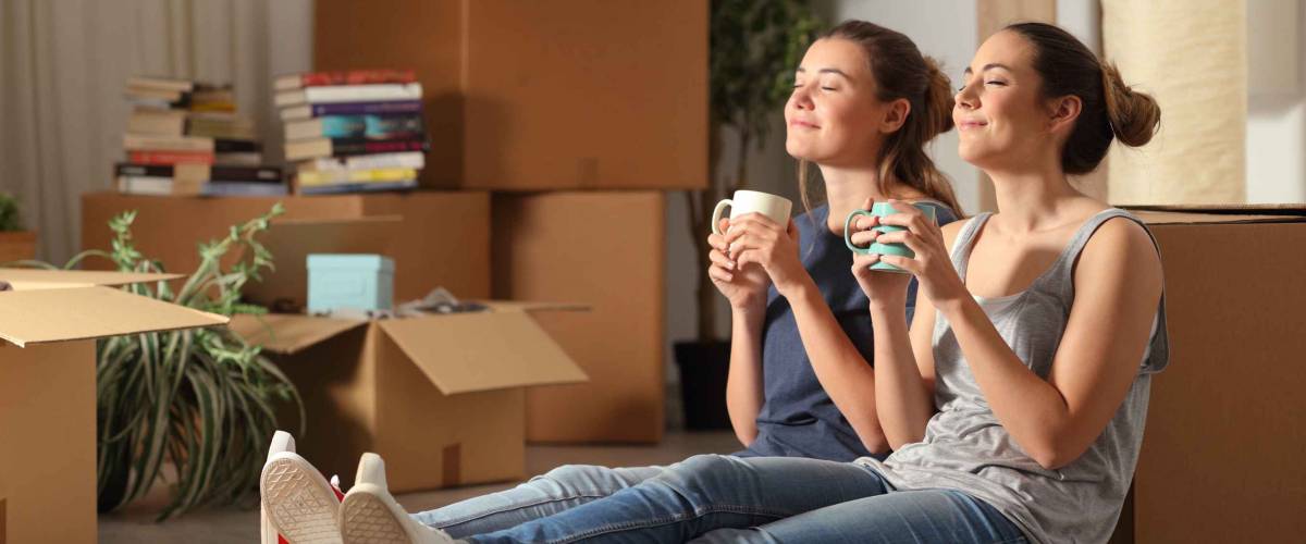 Two happy roommates moving home resting breathing fresh air sitting on the floor in the night