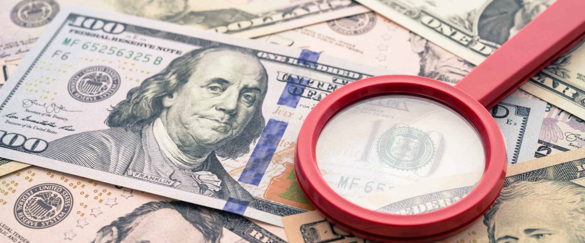 Red magnifying glass on US dollars paper banknote bill background.