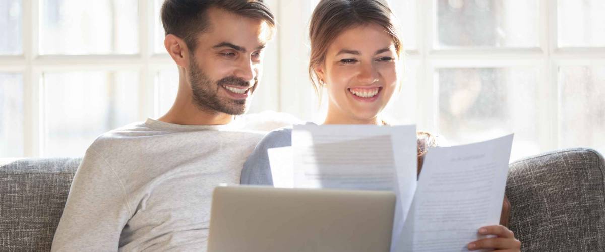 man and woman sitting on a couch, looking happy, going through papers