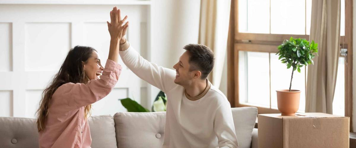 happy couple high five on couch, surrounded by boxes