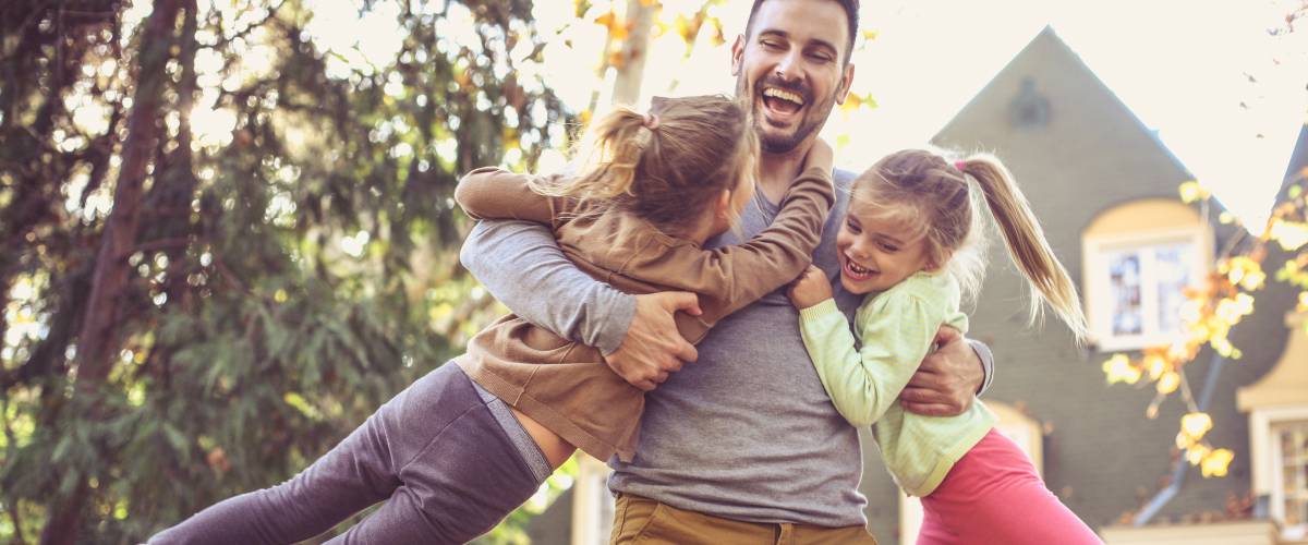 Man swings daughters around in his arms outside of home