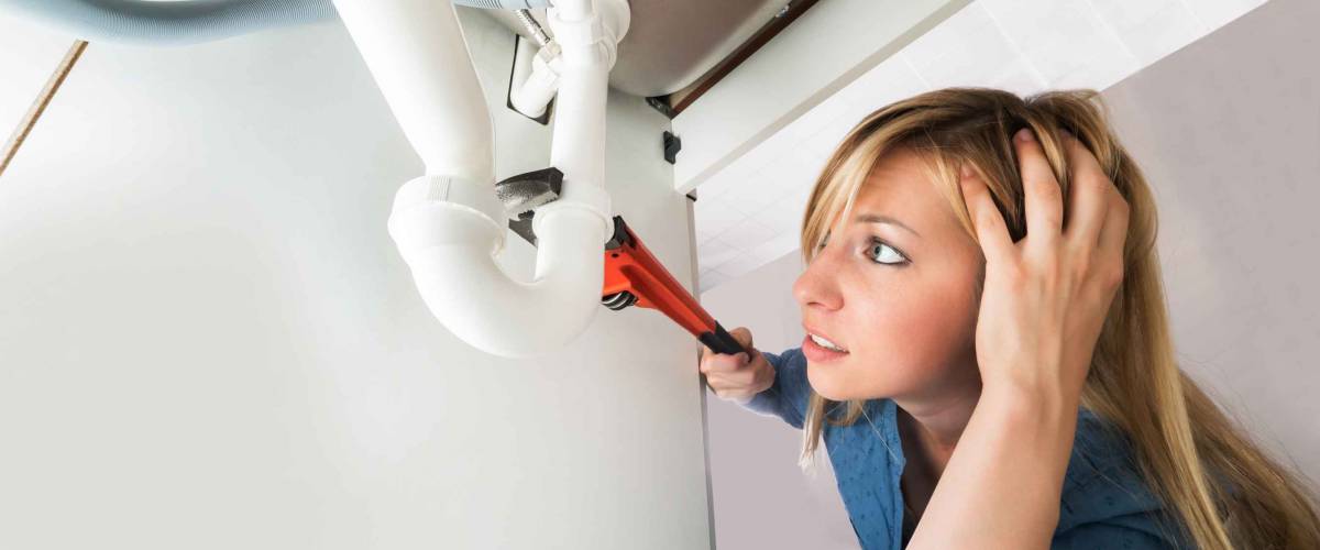 Woman with wrench trying to fix pipes under sink