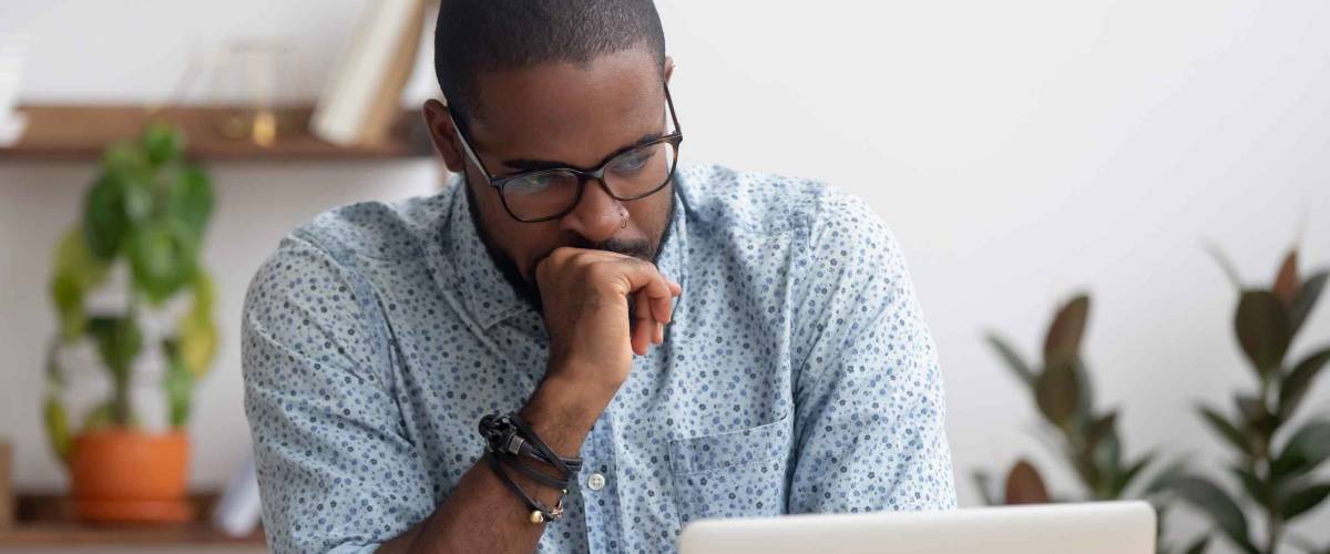 man looks serious with fist on his chin, while looking at a laptop