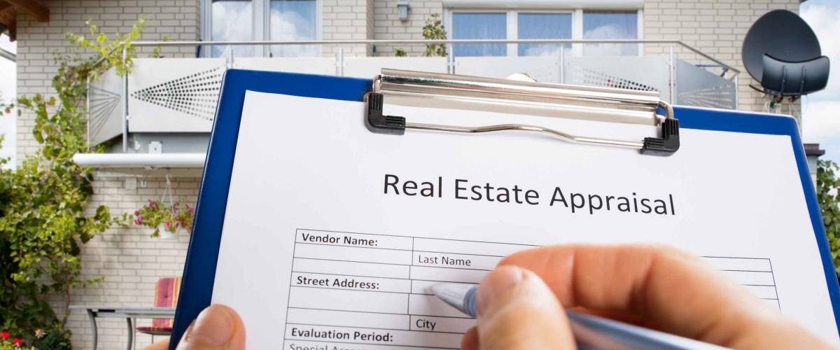 Close-up Of Person Hand Filling Real Estate Appraisal Document In Front Of House