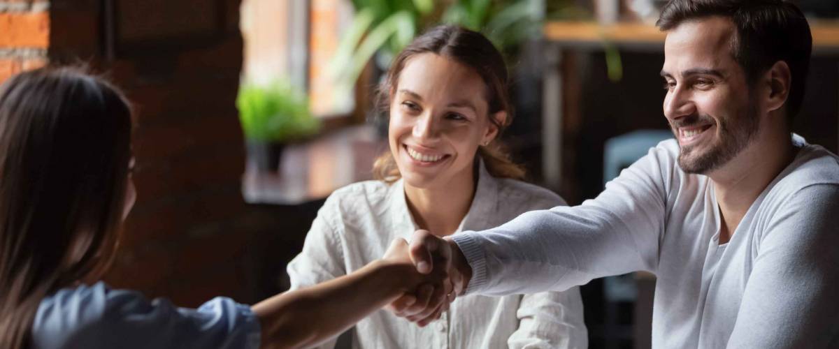 Smiling couple shake hands with woman across the table
