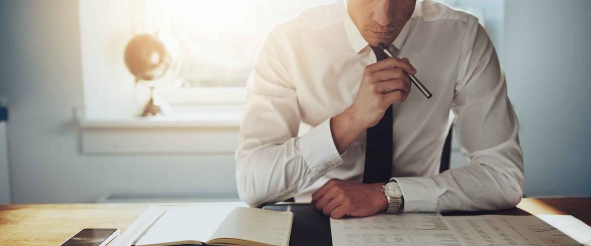 Serious business man working on documents looking concentrated with briefcase and phone on the table