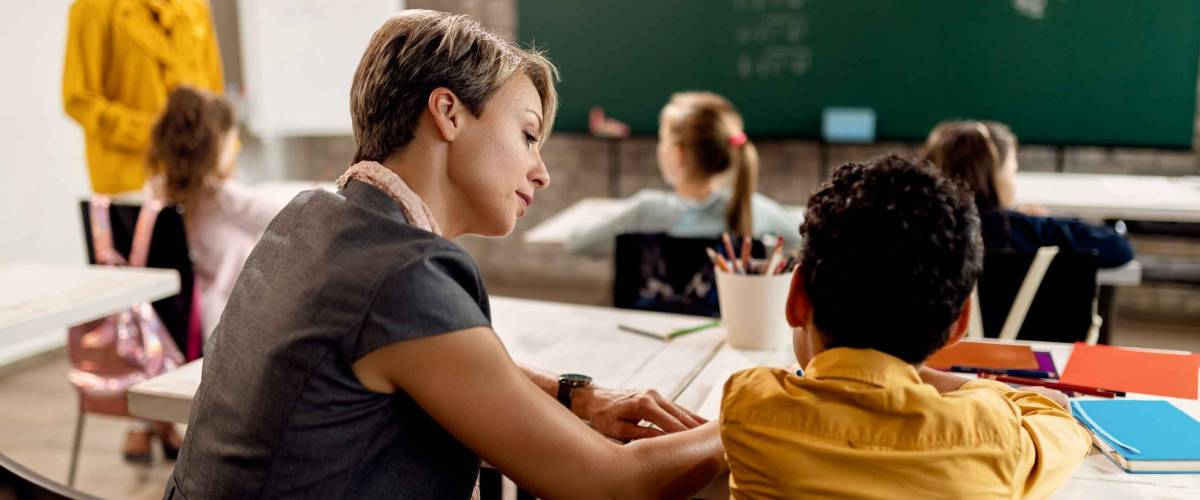 Female teacher helping elementary student with studying in the classroom.