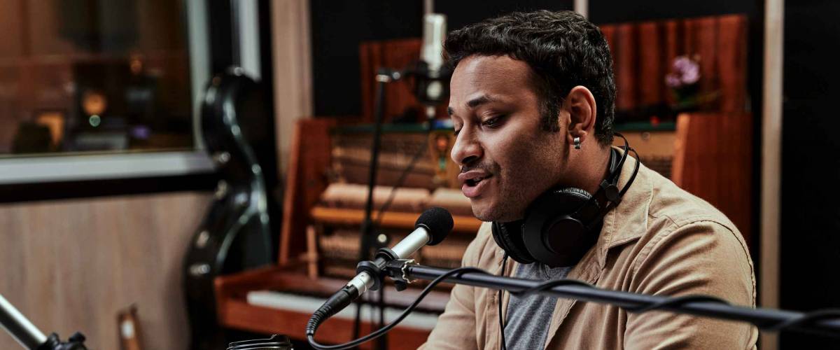 Portrait of young male radio host having a drink, looking focused while speaking in microphone, moderating a live show