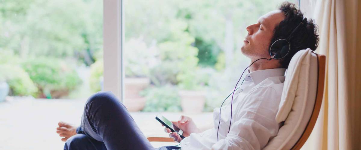 listening relaxing music at home, relaxed man in headphones sitting in deck chair in modern bright interior