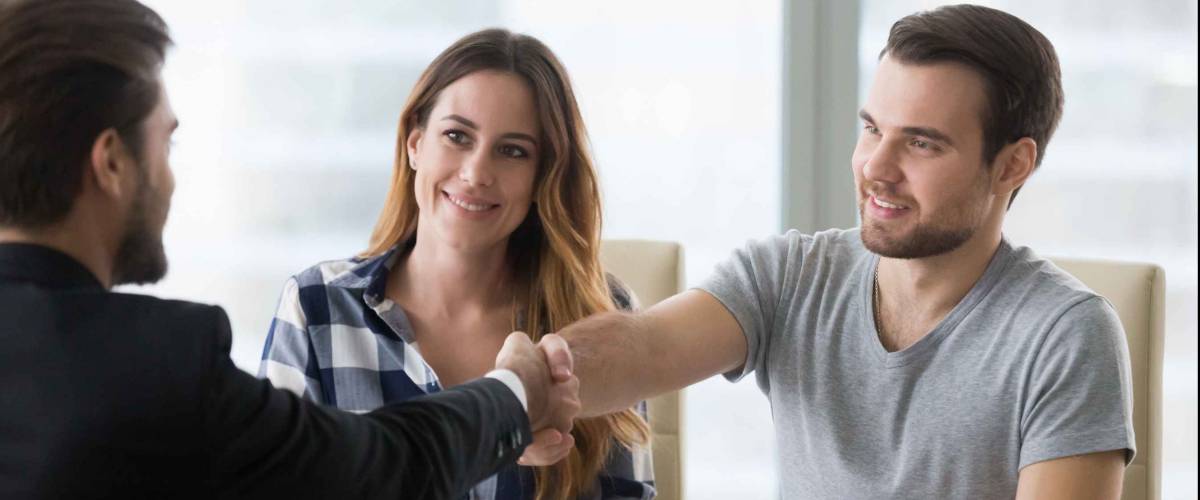 man and woman sit on one side of table, man shakes hand with other man on the other side