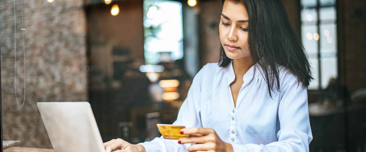 woman sitting with credit card in one hand, other on a laptop