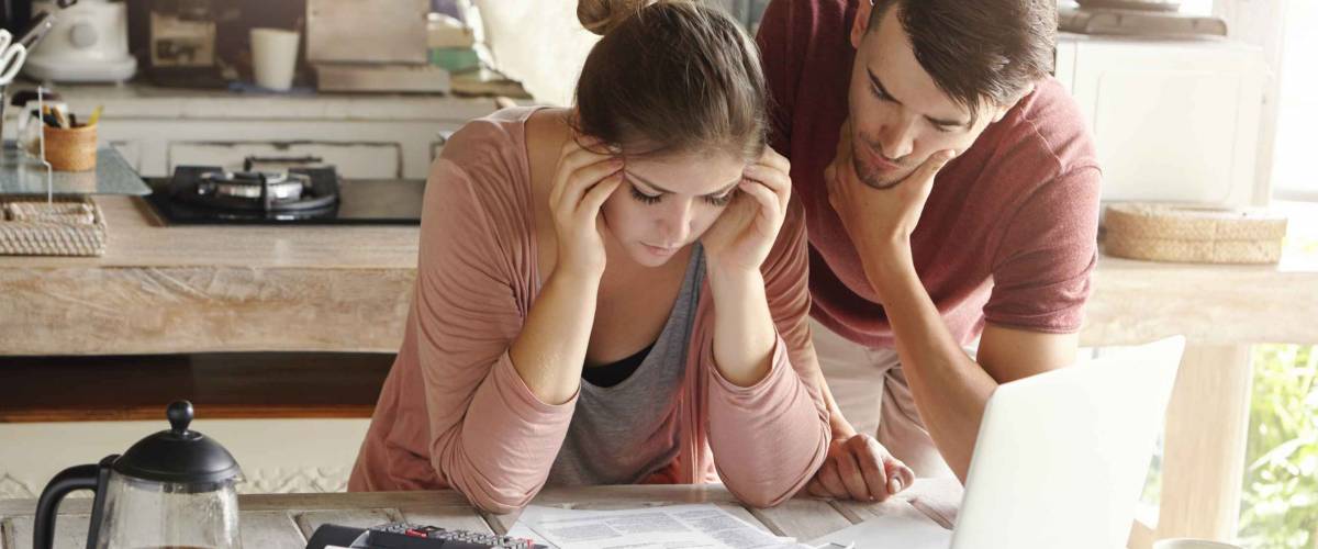Stressed young couple looking at papers on kitchen counter, holding heads in hands