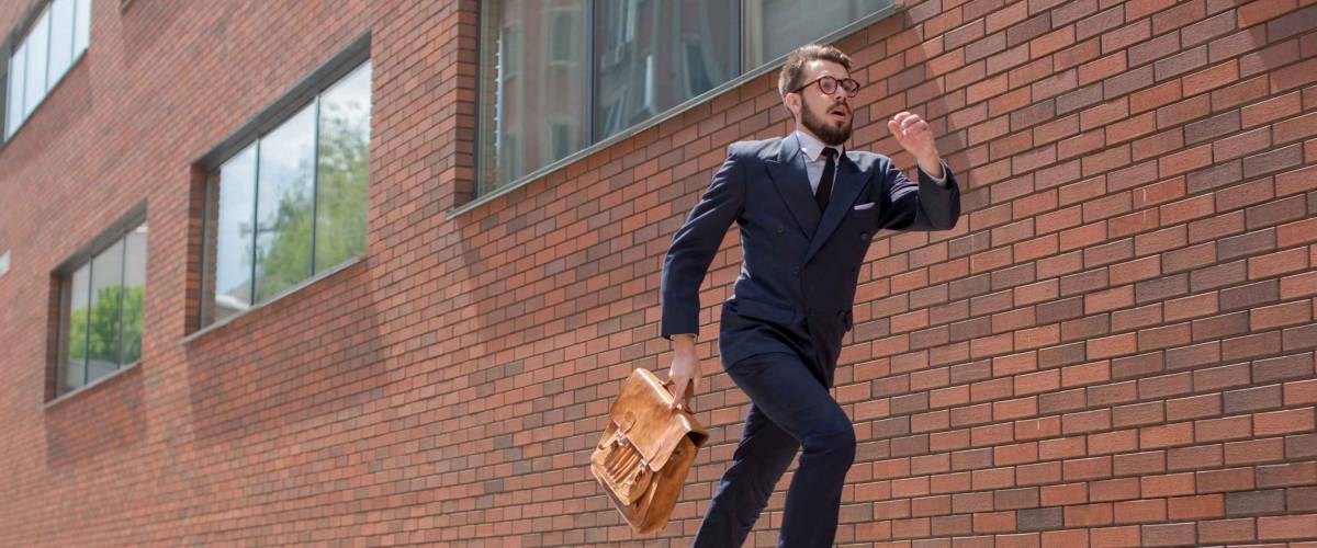 Young businessman with a briefcase and glasses running in a city street on a background of red brick wall