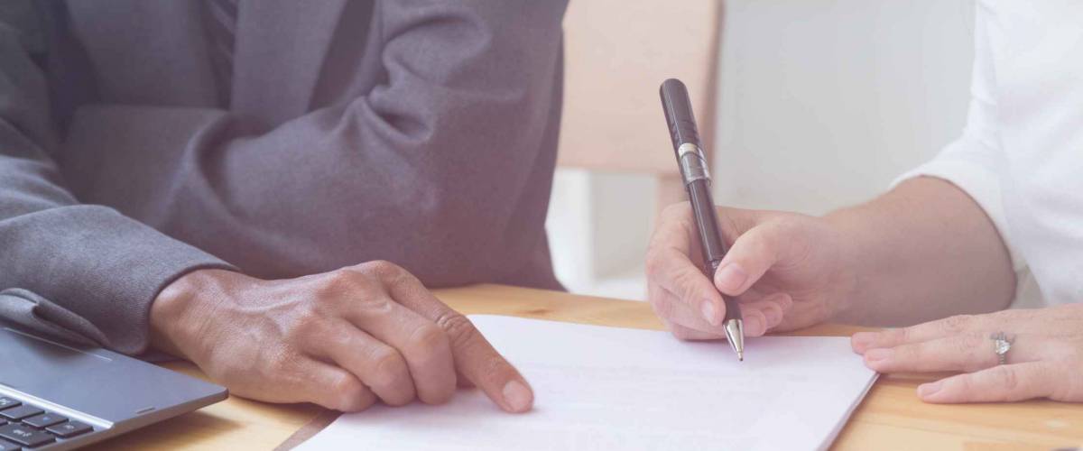 woman's hand hold ballpoint pen writing on paper sheet, while man points at spot on page