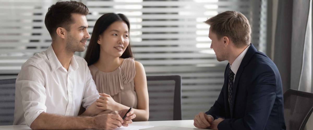 man in suit talking with young couple in professional setting