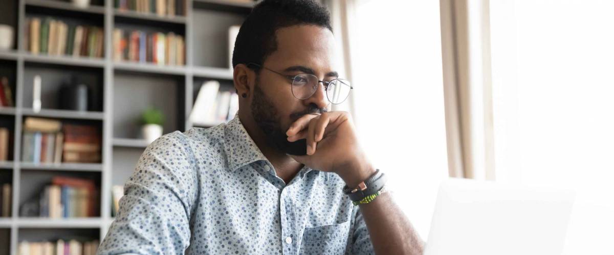 Focused young man sits in office, looks at laptop, hand over his mouth