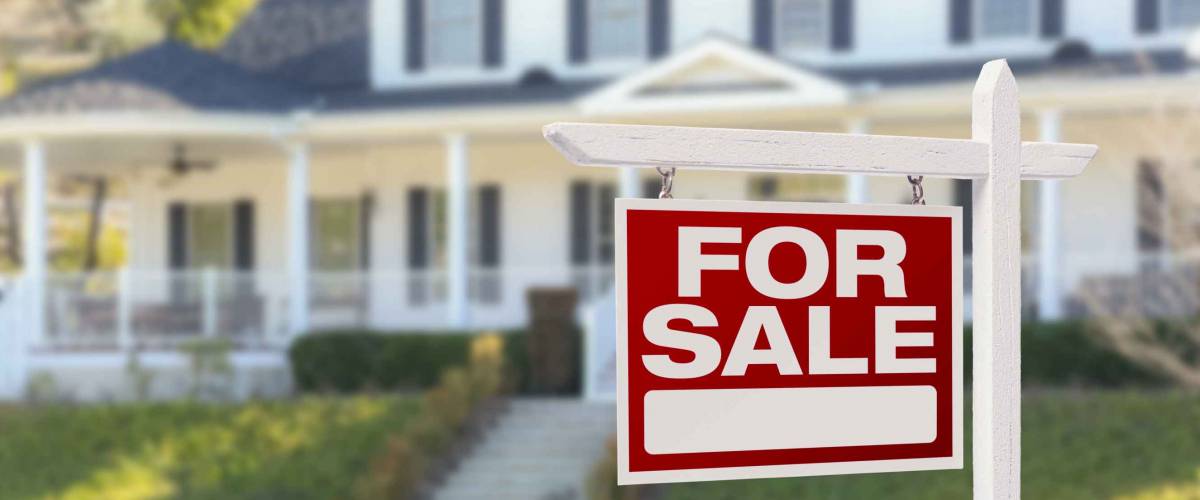 big white house with red for sale sign in front of it