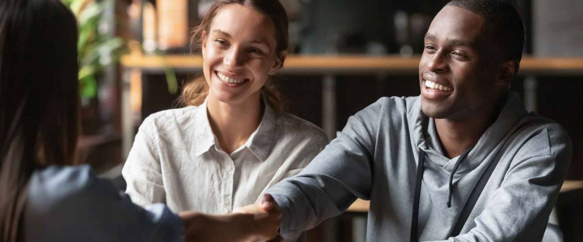 Happy young couple shake hand of woman sitting across from them at a table